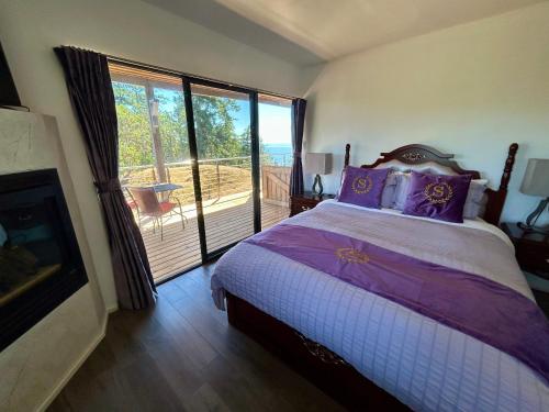a bedroom with a bed and a fireplace and a balcony at Shangri-La Oceanfront vacation home in Pender Island