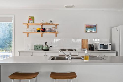 a white kitchen with a sink and two chairs at The Shack at Maslin Beach - C21 SouthCoast Holidays in Maslin Beach