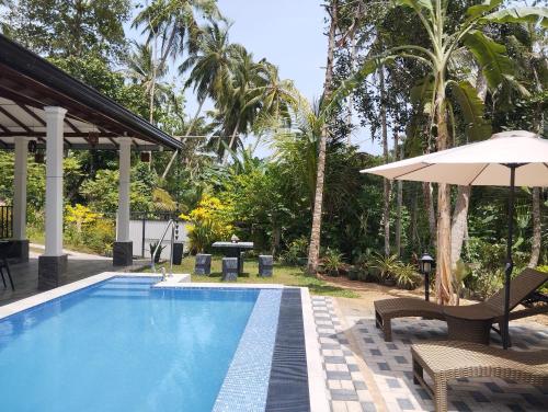 a swimming pool with an umbrella and chairs and a table at Serene Bliss Villa in Unawatuna