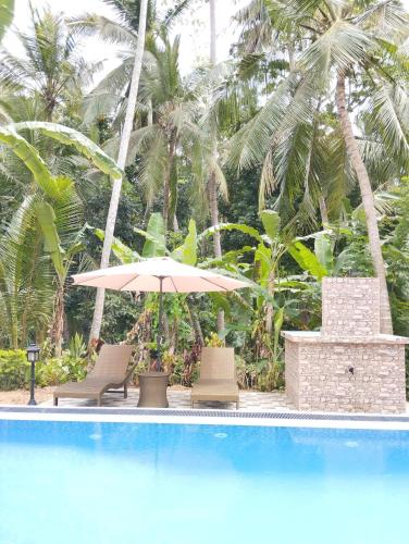 a pool with chairs and an umbrella and palm trees at Serene Bliss Villa in Unawatuna