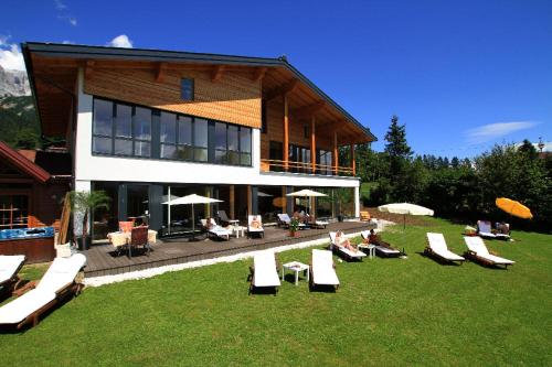 a building with lounge chairs and umbrellas in the grass at Landhaus Ramsau in Ramsau am Dachstein