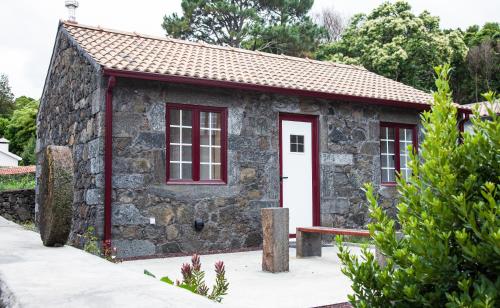a small stone building with a red door and windows at Aldeia das Adegas in São Roque do Pico