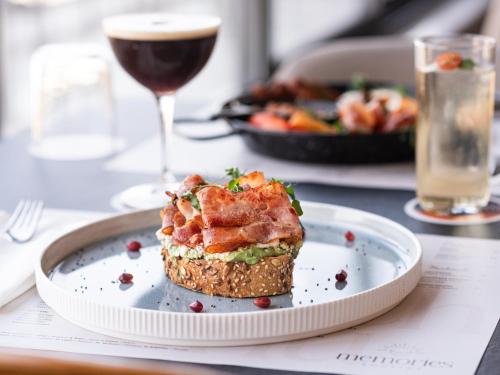 a plate with a sandwich on a table with a glass of wine at Rise Urban Art Hotel in Larnaka