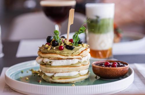 a stack of pancakes on a plate with a glass of wine at Rise Urban Art Hotel in Larnaka