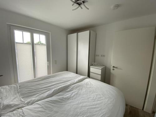 a white bedroom with a bed and a window at Come In Haffkrug in Haffkrug
