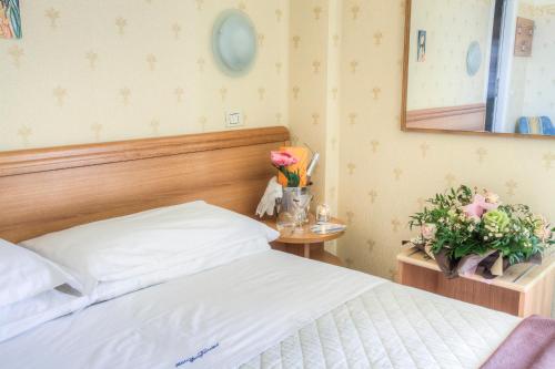 a bedroom with a bed and a mirror and flowers at Hotel San Francisco Spiaggia in Rimini