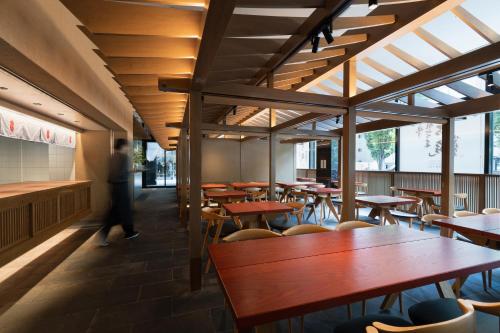 a restaurant with wooden tables and chairs and a person at Mitsui Garden Hotel Fukuoka Gion in Fukuoka