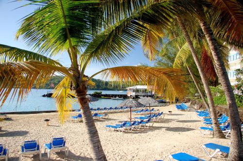 una playa de arena con sillas, palmeras y un cuerpo de agua en Carayou Hotel & SPA, en Les Trois-Îlets