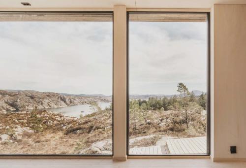 a room with two large windows looking out at a lake at Architect-Designed Cabin Panoramic View in Ervik
