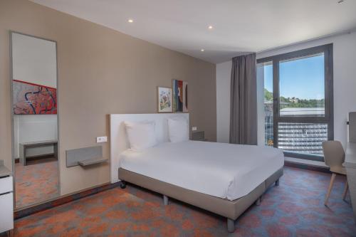 a bedroom with a white bed and a large window at Spark by Hilton Lyon Park Saone in Lyon