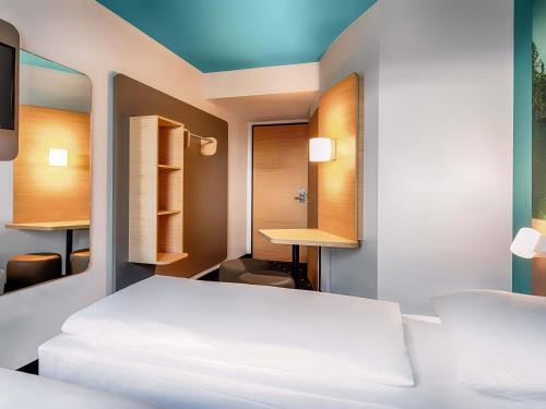a bedroom with a white bed and a desk at B&B Hotel München-Putzbrunn in Putzbrunn