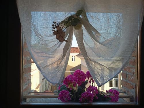 a window with a curtain and flowers on a window sill at La Mansardina di Sabrina in Busca