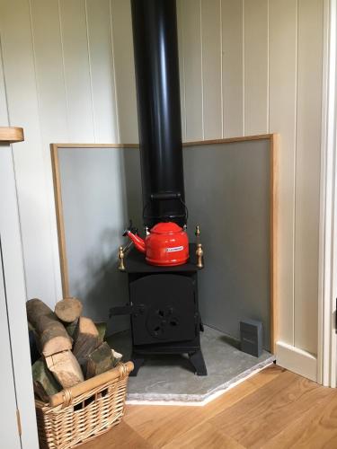a wood stove with a red pot on top of it at The Scrumpy Shepherd, Brandeston in Cretingham