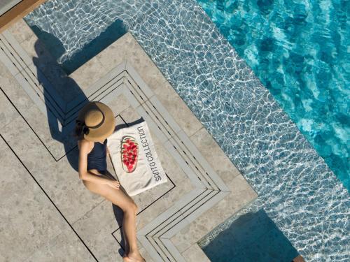 a woman in a hat standing next to a swimming pool at Santo Pure Oia Suites & Villas in Oia