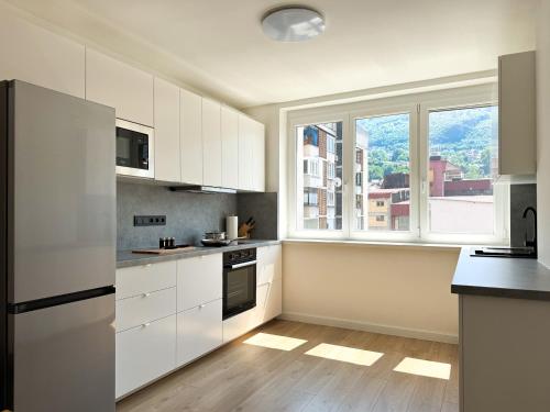 サラエボにあるBright modern apartment, 100m from Sarajevo City Hall & Old Townの白いキャビネットと大きな窓のあるキッチン