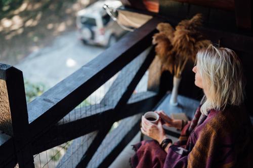 a woman sitting on a bench holding a cup of coffee at Rent a Forest, Cabin Hidden in the Fruška gora in Velika Remeta