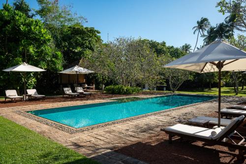 a swimming pool with chairs and umbrellas next to it at Nyne Hotels Rock Villa - Bentota in Bentota