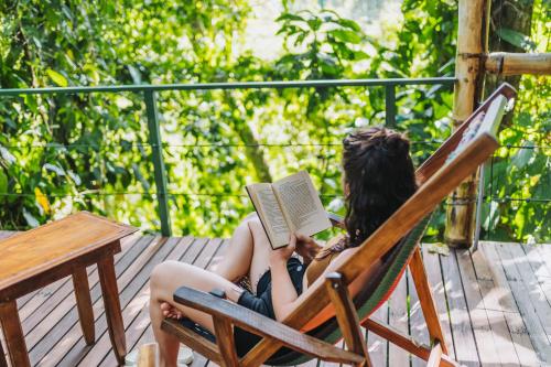 a woman sitting in a chair reading a book at Colina Secreta - Glamping and Villas in Puerto Viejo