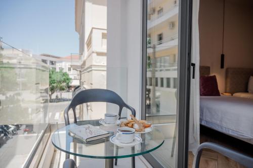 a glass table with a chair and coffee cups and pastries at IRA - ΗΡΑ Hotel in Kalamata