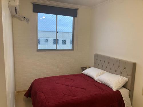 a bedroom with a bed with a red blanket and a window at Apartamento em Gravataí in Gravataí