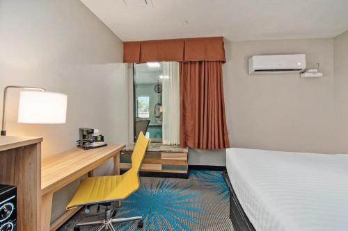 a hotel room with a bed desk and a yellow chair at Days Inn & Suites by Wyndham Mt Pleasant in Mount Pleasant