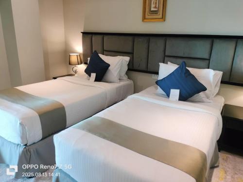 two beds in a hotel room with blue pillows at City Point Hotel in Manama