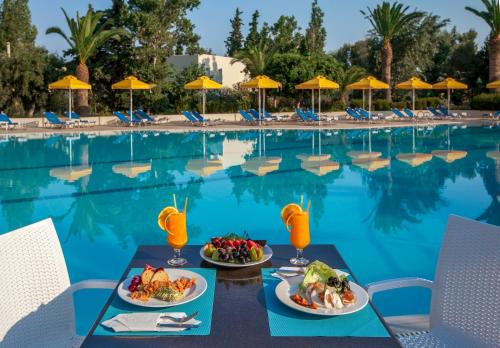 a table with two plates of food next to a swimming pool at Kipriotis Hippocrates Hotel in Kos Town