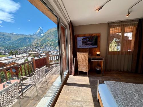 a room with a balcony with a bed and a desk at Alpenlodge in Zermatt