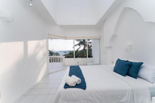a white bedroom with a large bed with blue pillows at 3067 - Casa Blanca in Tangolunda