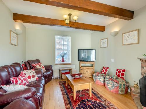 a living room with a leather couch and a tv at Curlew Cottage in Caister-on-Sea