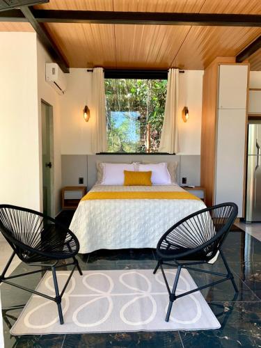 a bedroom with a bed with two chairs and a window at Piribless Chalés - Diamond in Pirenópolis