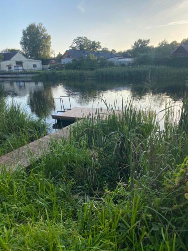 a river with a dock and a boat in the water at Gulbės Apartamentai in Anykščiai