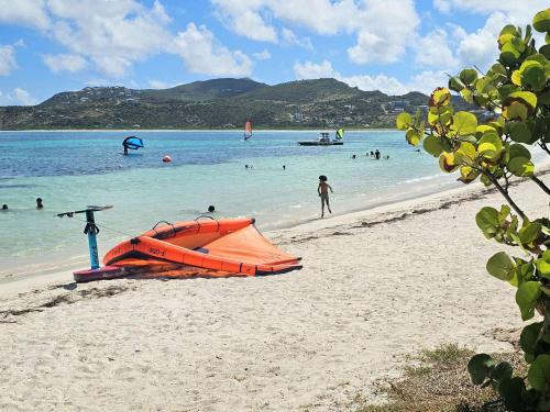 an orange boat on a beach with people in the water at Studio spacieux à Baie Orientale avec piscine et parking - FR-1-734-31 in Cul de Sac