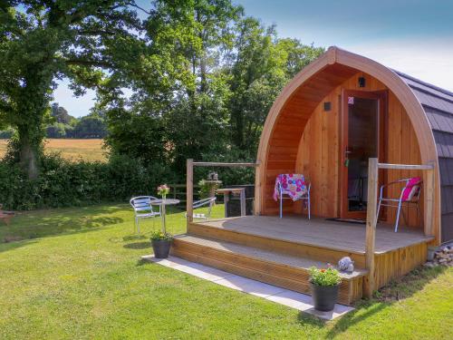 a small wooden cabin with a porch and a table and chairs at Barley Hill Pod in Broadway