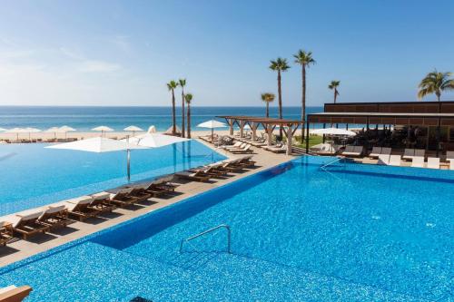 a swimming pool with chairs and the ocean in the background at Altitude by Krystal Grand Los Cabos - All Inclusive in San José del Cabo