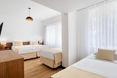 a white bedroom with two beds and a desk at Savoy Othon Lite in Rio de Janeiro