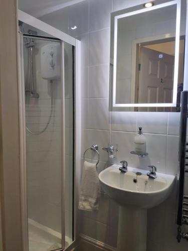 a bathroom with a sink and a shower with a mirror at The Rosedene in Llandudno