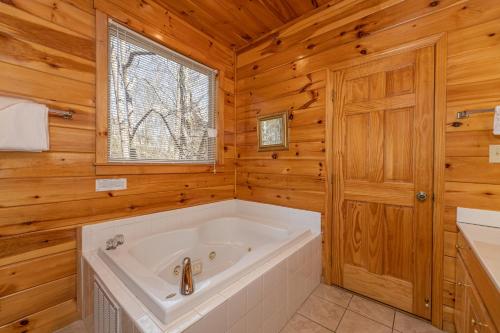 a white tub in a wooden bathroom with a window at HIckernut Lodge by American Patriot Getaways in Walnut Grove