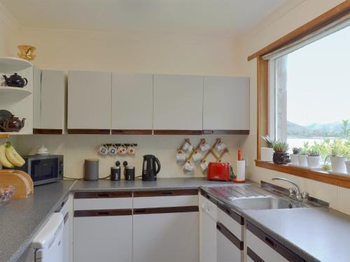 a kitchen with white cabinets and a sink and a window at Dunyvaig in Colintraive