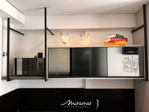 a kitchen with black and white cabinets and a microwave at Get By Side - Jardim Oceania in Tambaú