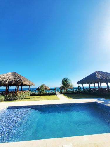 a swimming pool with straw umbrellas and the ocean at Serendipia Hotel Nizao in Nizao