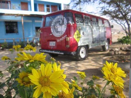 a red van parked in a yard with yellow flowers at My Friend Surf Hostal in Trujillo
