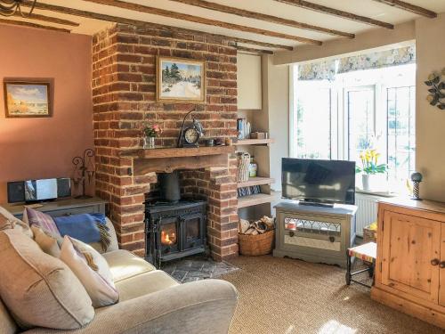 a living room with a brick fireplace and a television at Beehive Cottage in Wittersham