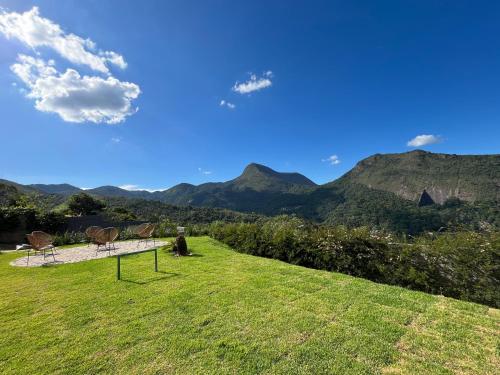 a field with two chairs and mountains in the background at Casa 02 Monte Boa Vista - Casa de 4 Suítes com Vista Deslumbrante in Teresópolis