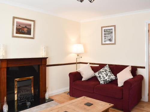 a living room with a red couch and a fireplace at Twizell Cottage in Alnwick