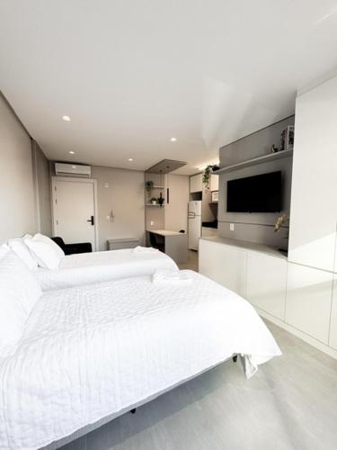 a white bedroom with two beds and a kitchen at Loft H1273 Apto 502 in Caxias do Sul