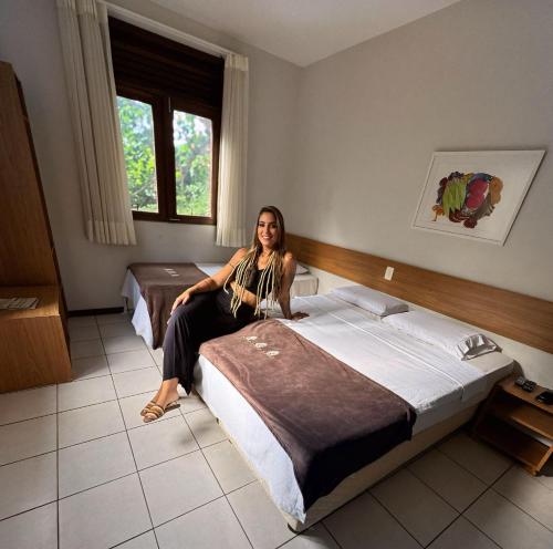 Una mujer sentada en una cama en una habitación de hotel. en Hotel Pedra da Concha, en Salvador