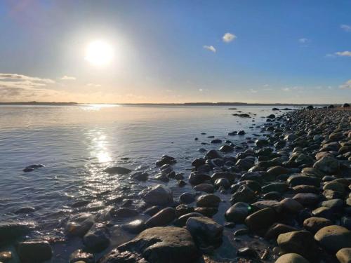 a rocky beach with the sun rising over the water at Luxury Seaside Retreat - By Traum Ferienwohnungen in Haderslev