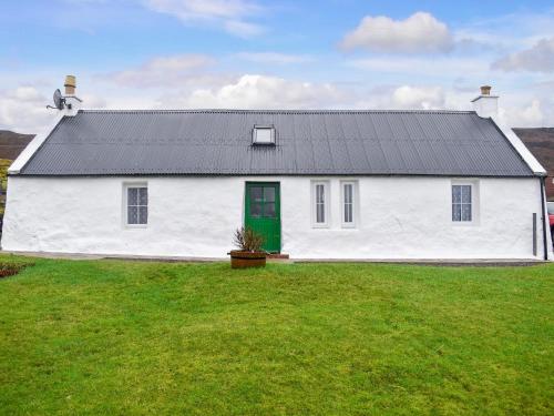 une maison blanche avec une porte verte sur un champ dans l'établissement The Cottage, à Ollach