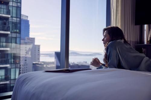 a woman sitting on a bed in a room with a window at Hotel Indigo Auckland by IHG in Auckland